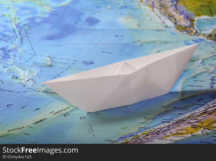 A white toy paperboat on a map. A white toy paperboat on a map.