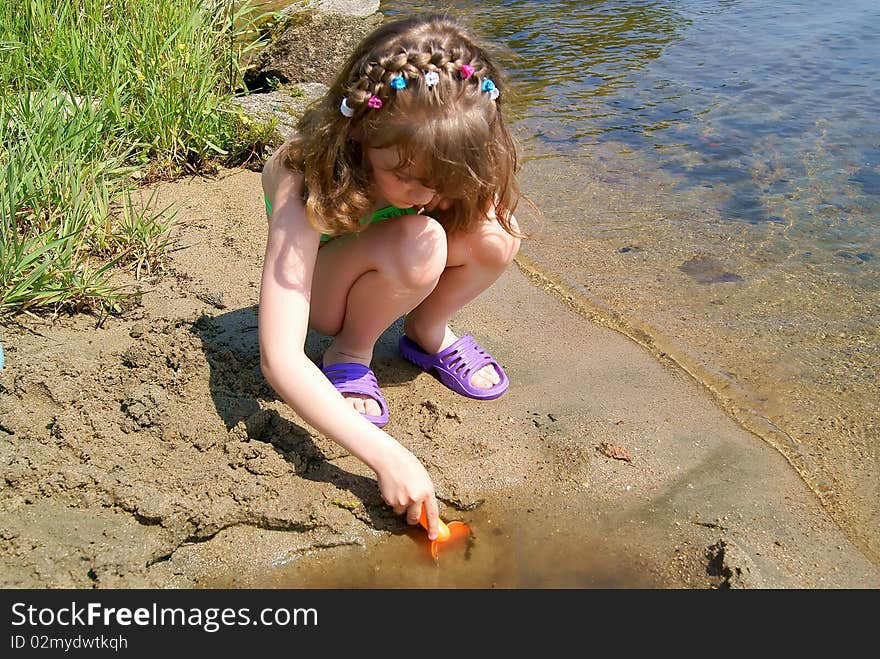 In the summer on the bank of lake the child plays sand at water. In the summer on the bank of lake the child plays sand at water