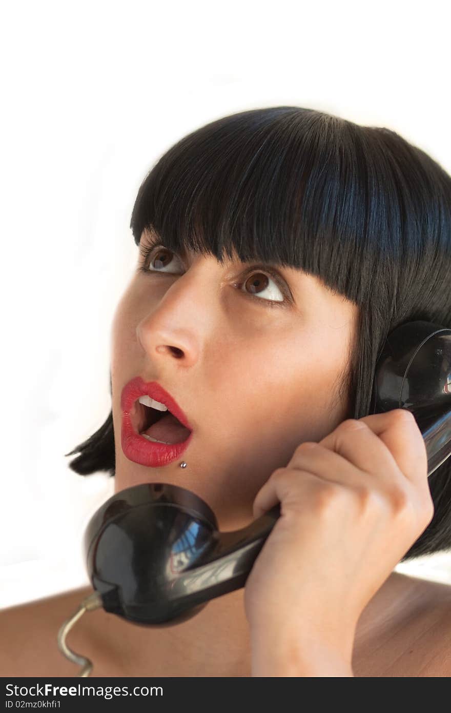 A young woman holds the telephone surprised at what she's listening from the other side, on white background. A young woman holds the telephone surprised at what she's listening from the other side, on white background