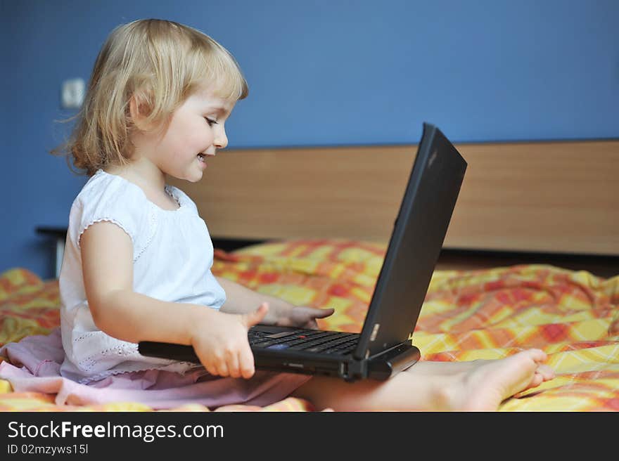 Cheerful little girl with laptop sits on bed of parents