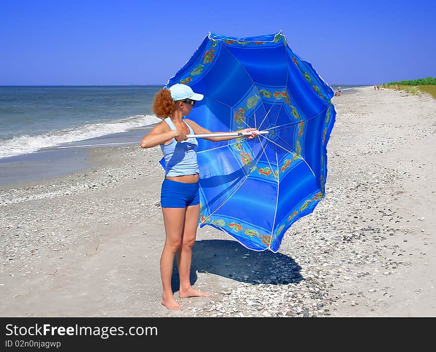 The woman opens the blue umbrella on the beach