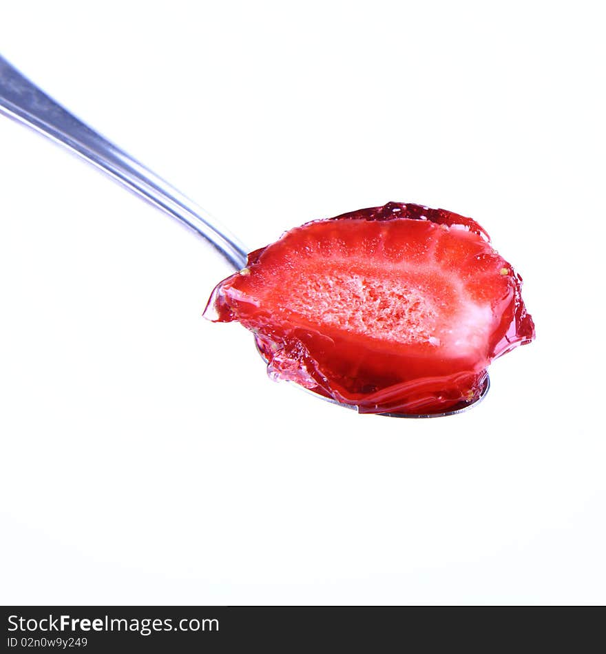 Piece of a strawberry covered with jelly on a spoon