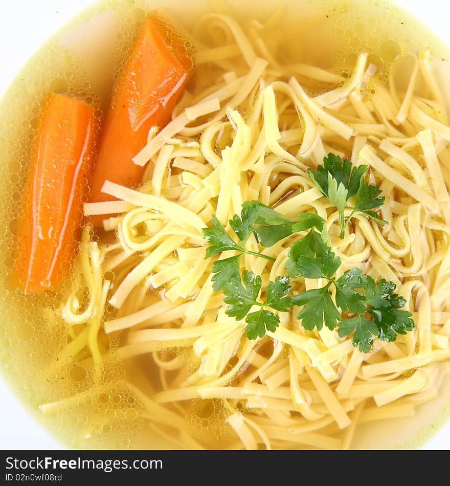 Chicken soup with macaroni and carrots decorated with parsley on a plate in close up