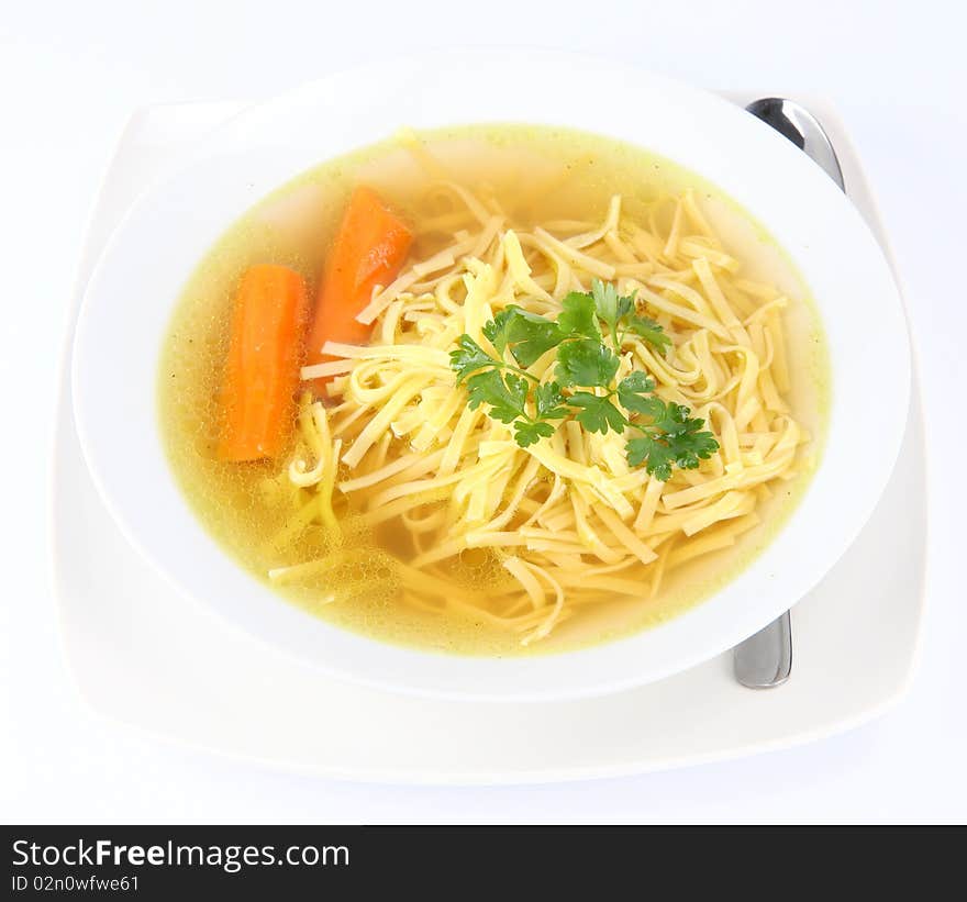 Chicken soup with macaroni and carrots decorated with parsley on a plate with a spoon