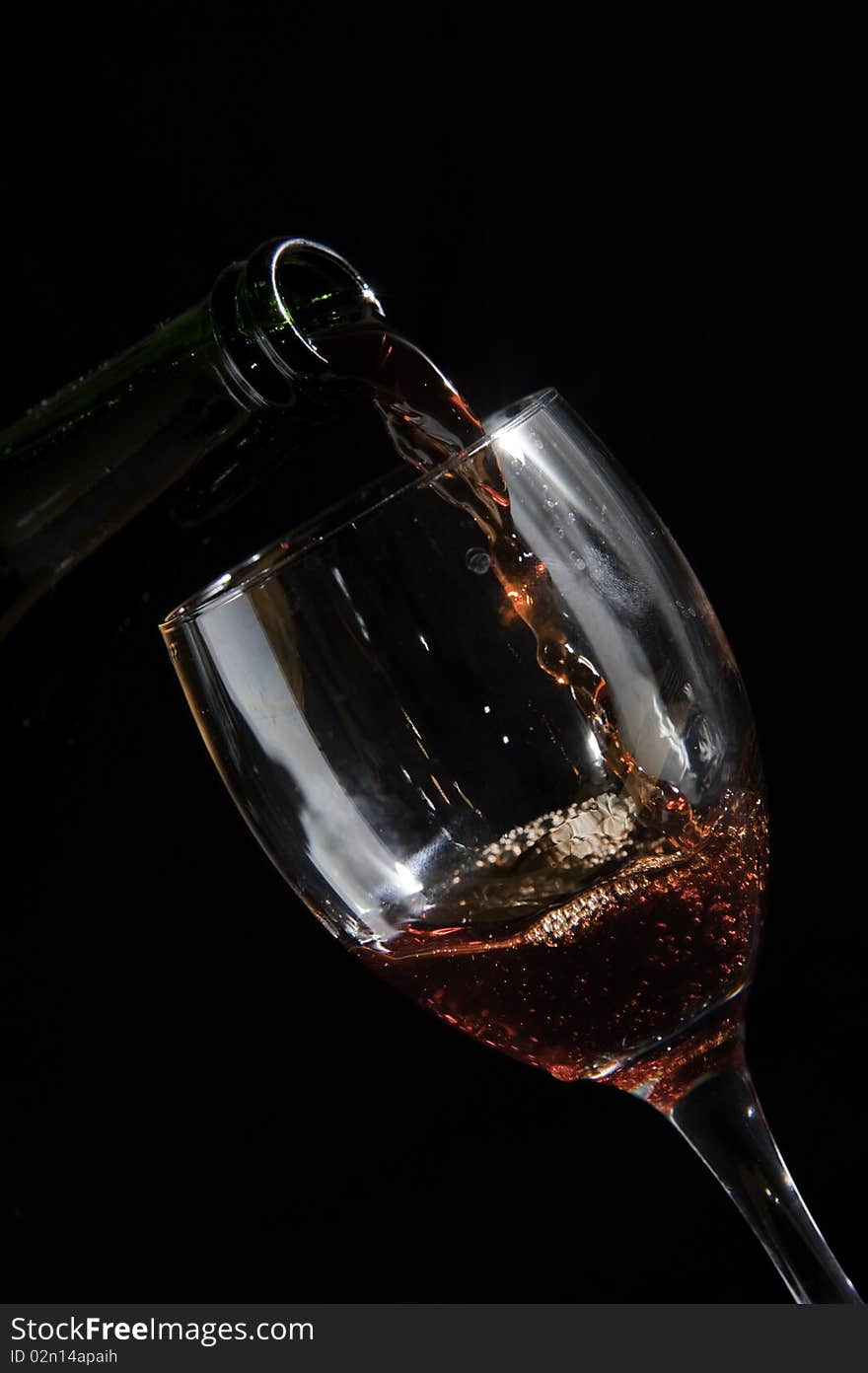 Photo of a glass and bottle pouring wine on black background, showing movement of the liquid. Photo of a glass and bottle pouring wine on black background, showing movement of the liquid