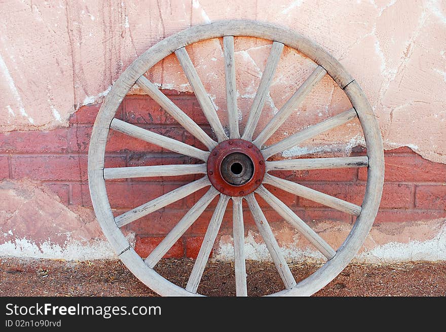 Old weathered wagon wheel leaning against brick wall. Old weathered wagon wheel leaning against brick wall