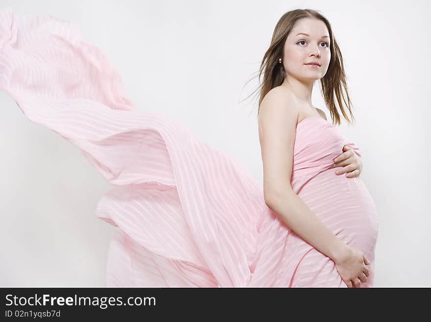 Young pregnant woman and pink flowing textile on white background. Young pregnant woman and pink flowing textile on white background.