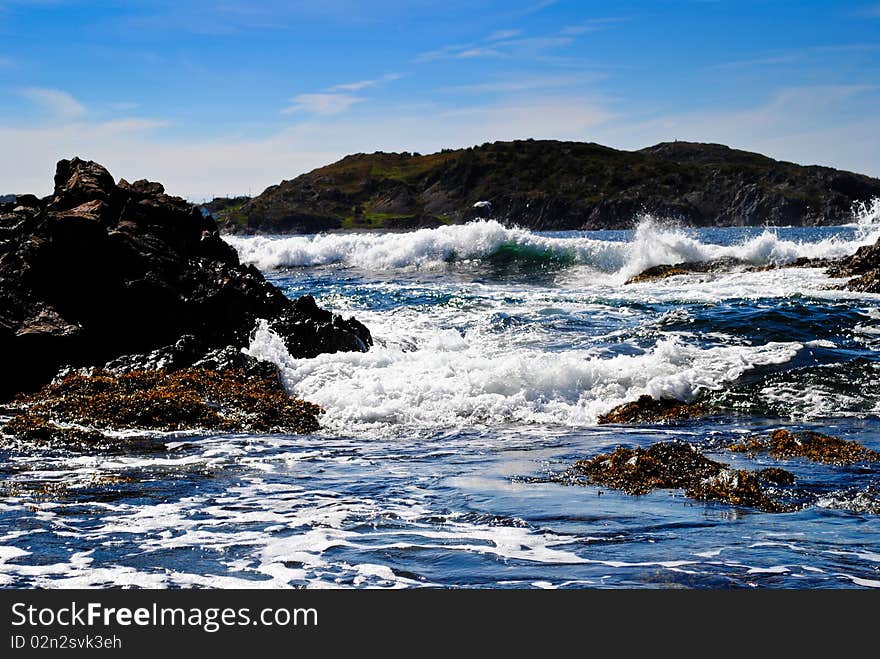 Waves crashing on rocks in Durrell bay in Twillingate newfoundland. Dark blue water and deep blue sky. Seeweed on water. Waves crashing on rocks in Durrell bay in Twillingate newfoundland. Dark blue water and deep blue sky. Seeweed on water