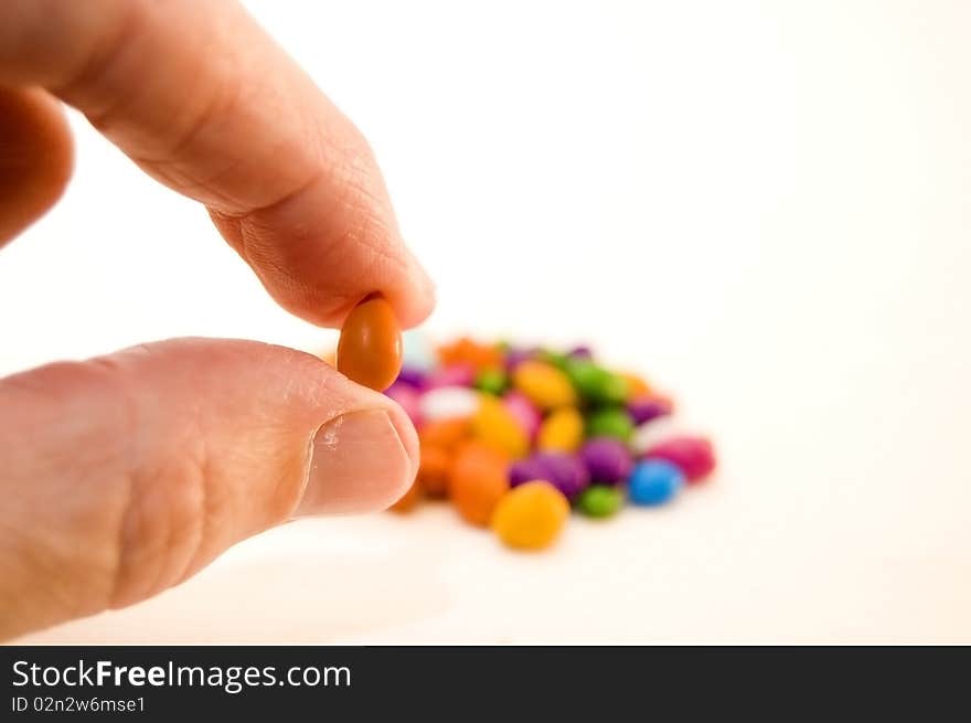 A man's hand holding a tiny piece of orange candy. A man's hand holding a tiny piece of orange candy