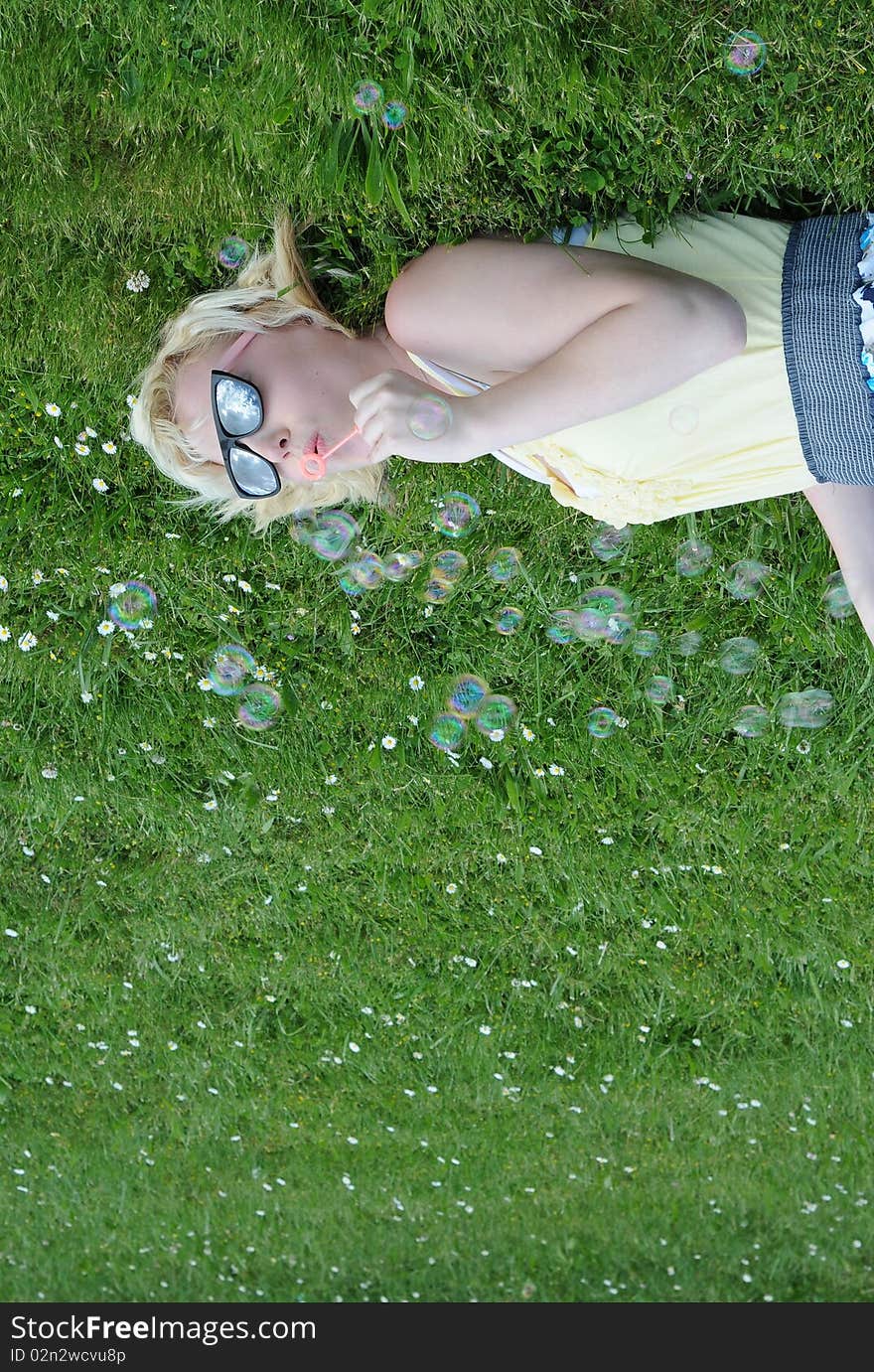 Young white Caucasian teenage girl laying in grass blowing bubbles with her sunglasses on, looking up at the sky. Young white Caucasian teenage girl laying in grass blowing bubbles with her sunglasses on, looking up at the sky.