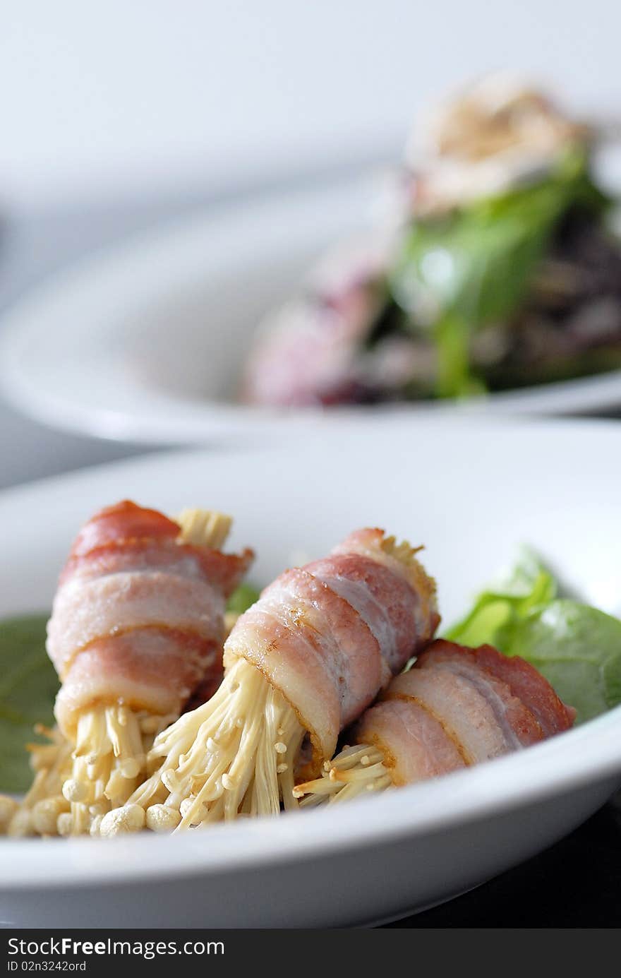 Bacon with Enoki mushroom served on plate with salad in background