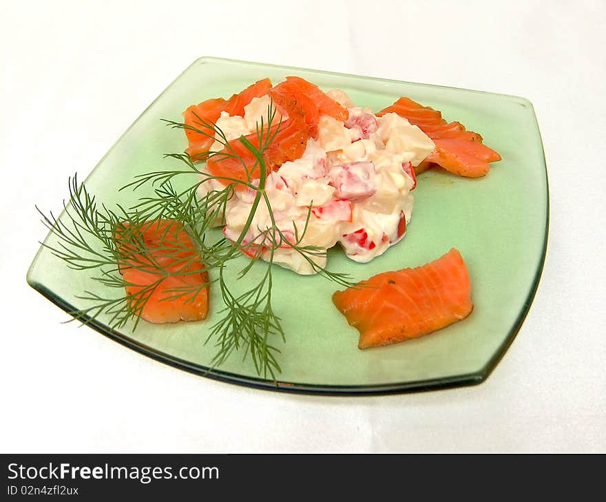 In the center of the green glass plates placed salad of boiled potatoes, soy sauce, tomato, egg, mayonnaise. The edges of the plates are pieces of salmon. The dish is decorated with a sprig of dill.