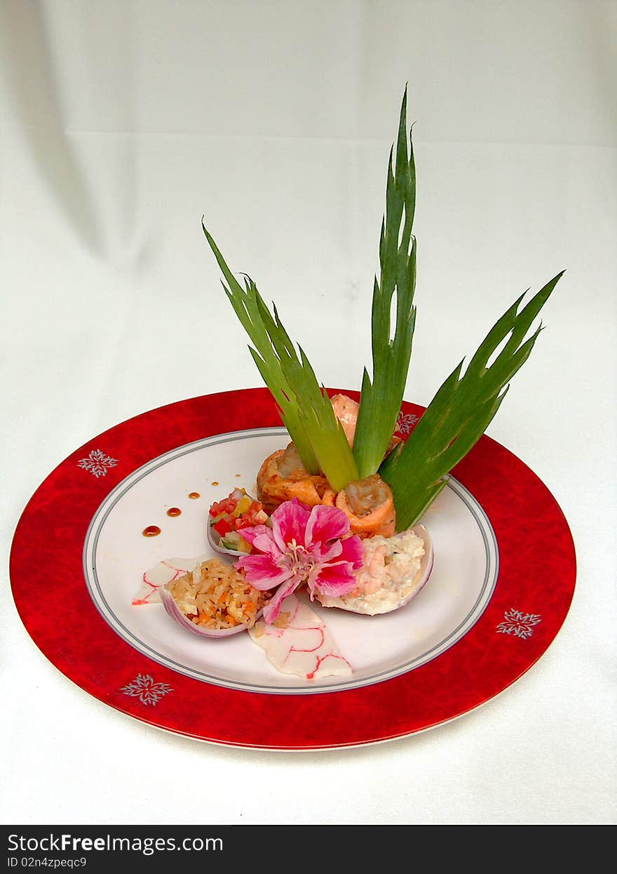 The fillet barracuda decorated salmon, green leaves and flower on the round plate with red border. The fillet barracuda decorated salmon, green leaves and flower on the round plate with red border.