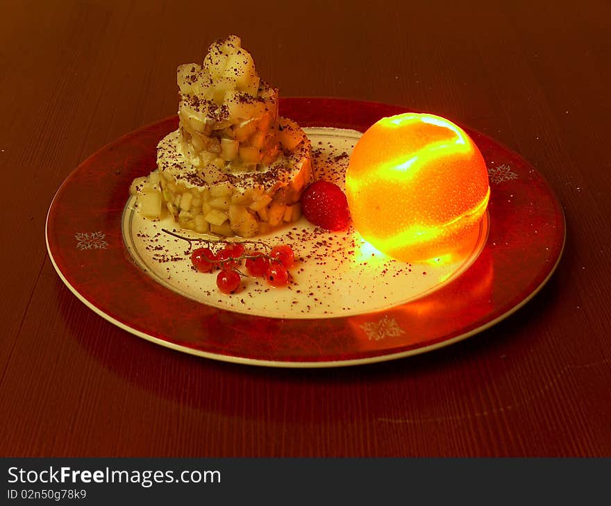 The red plate of fruit dessert. This fruit dessert is collected in three-storey a pyramid and decorated with wood berry. The cut peel of an orange is collected in the whole, inside it burns small candle. The red plate of fruit dessert. This fruit dessert is collected in three-storey a pyramid and decorated with wood berry. The cut peel of an orange is collected in the whole, inside it burns small candle.