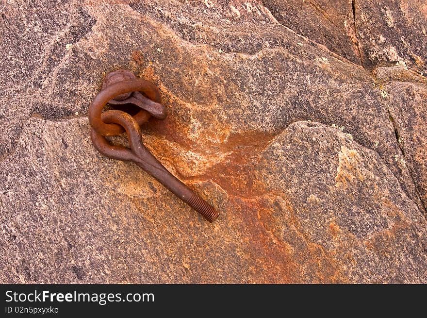 Rusty metal anchor on a rock covered with red iron oxide.