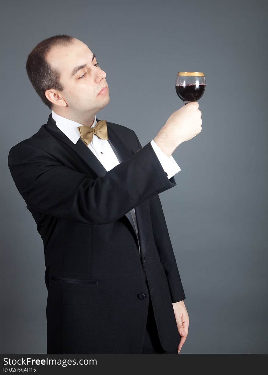 Man in tuxedo looking at the glass filled with red wine. Man in tuxedo looking at the glass filled with red wine.