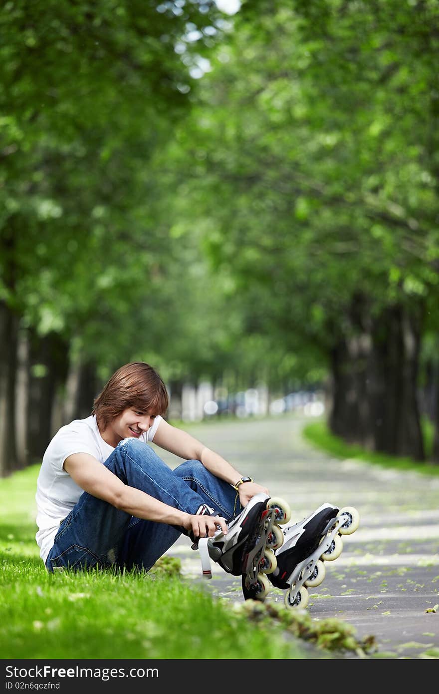 The young guy fastens rollers on a grass in park. The young guy fastens rollers on a grass in park