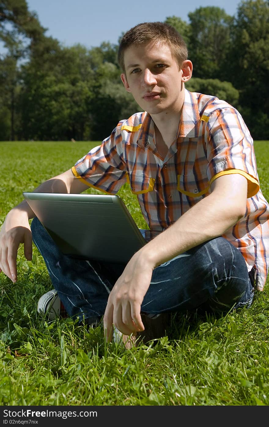 Young man sitting on green grass in park and types on laptop. Young man sitting on green grass in park and types on laptop