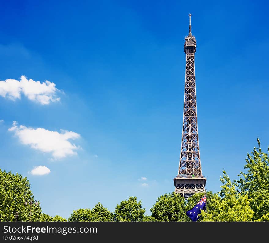 Eiffel Tower, with cloudy blue sky and sunny trees around.