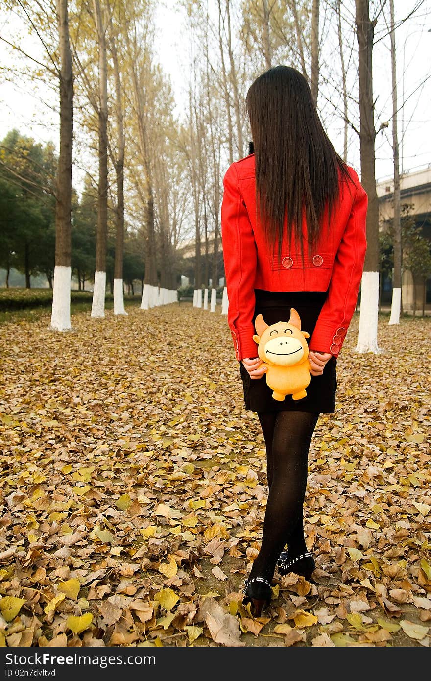 Beautiful girl walking on defoliation,in red coat,puppet in hands