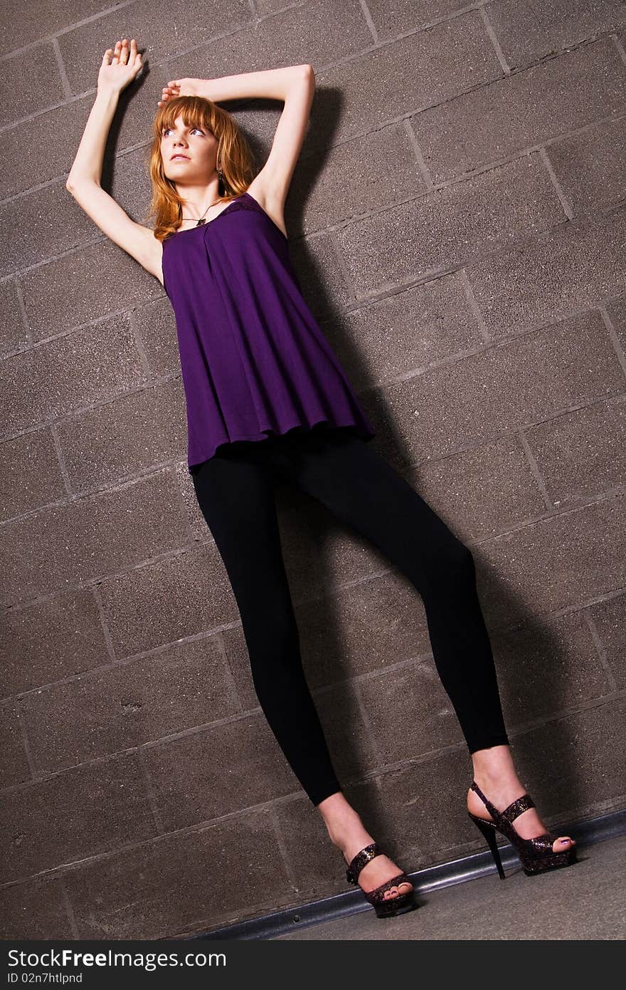 Fashionable red-haired woman posing near the brick wall