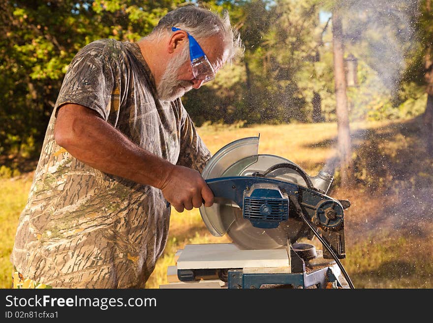 Active older man working with an electric saw in the yard. Active older man working with an electric saw in the yard.