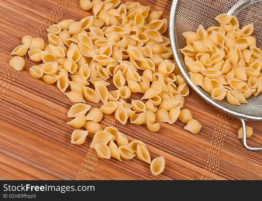 Dry shell pasta on bamboo mat with strainer. Dry shell pasta on bamboo mat with strainer