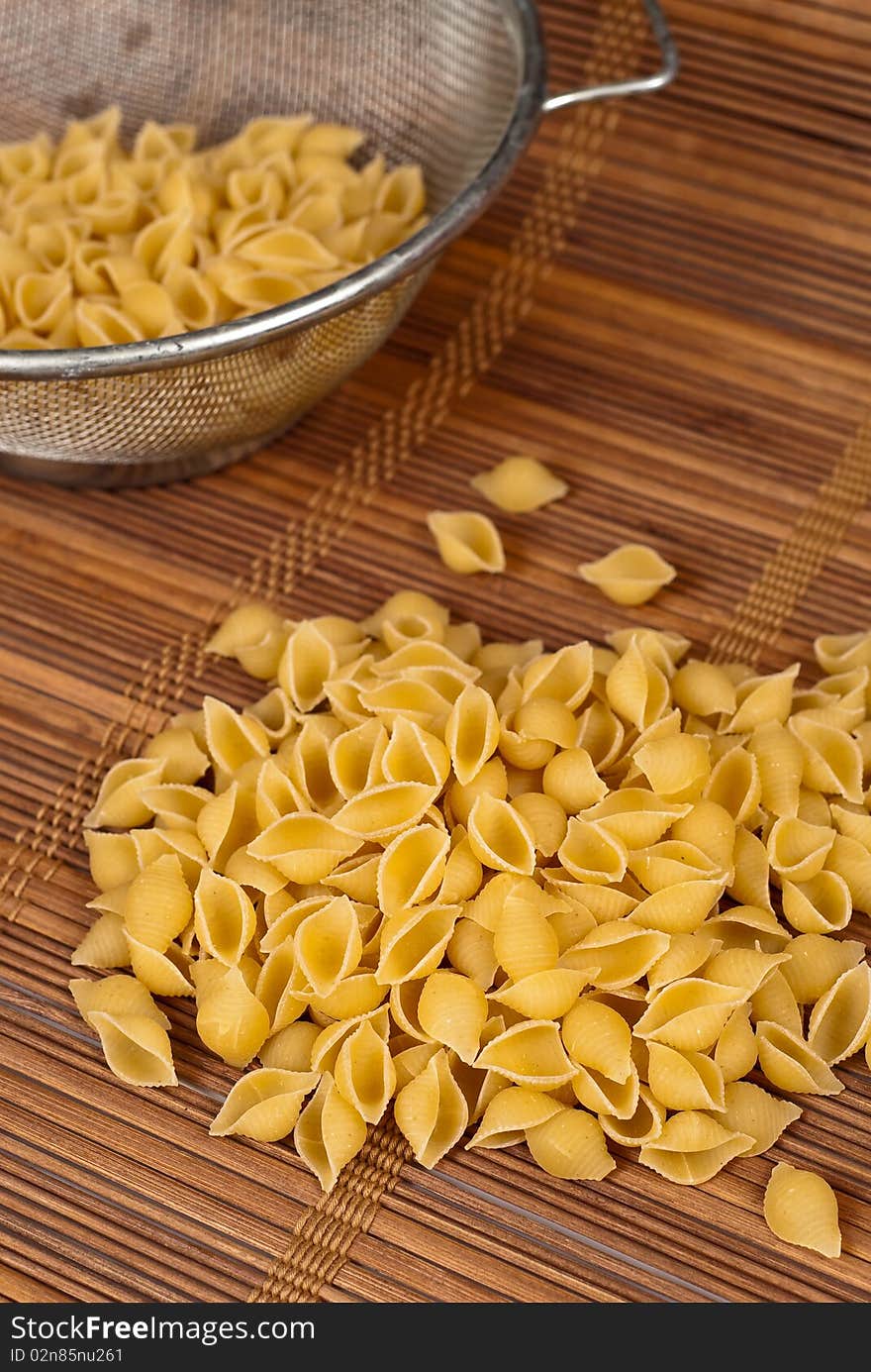 Dry shell pasta spilled out of a strainer. Dry shell pasta spilled out of a strainer