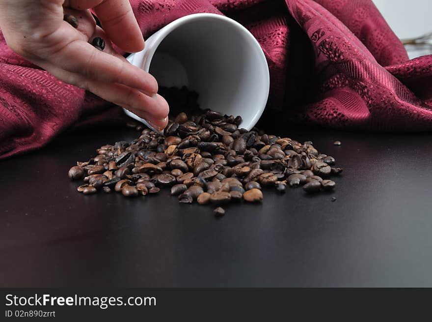 Coffee granules on black table with cup and hand with red velvet scarf