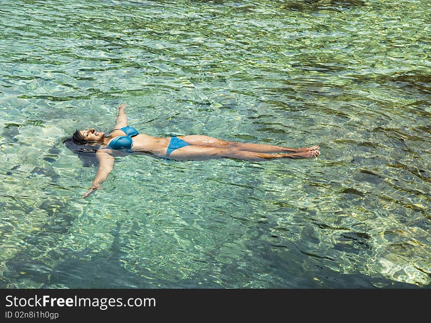 A color photo of a beautiful indian woman relaxing as she floats in the clear blue colored sea while wearing a bikini during her summer vacation. A color photo of a beautiful indian woman relaxing as she floats in the clear blue colored sea while wearing a bikini during her summer vacation.