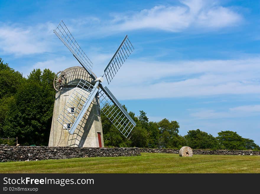 Historic New England windmill behind a stone fence and in a grassy field. Historic New England windmill behind a stone fence and in a grassy field