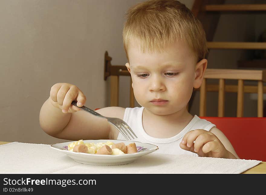 Small cute boy eats his dinner himself. Small cute boy eats his dinner himself