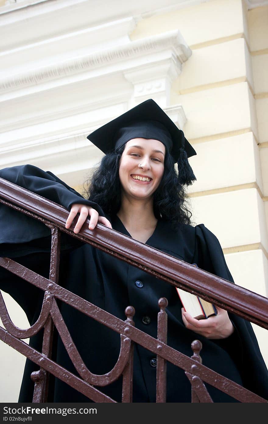 Young laughing student in gown near the university