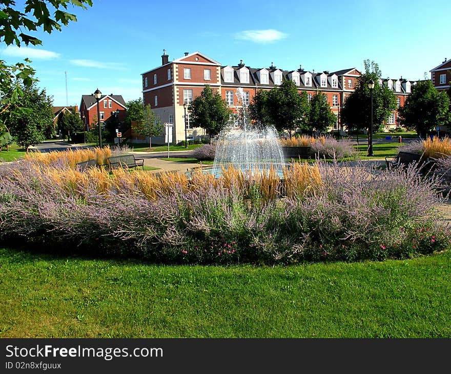 A fountain in a gardin surrounded by town homes.