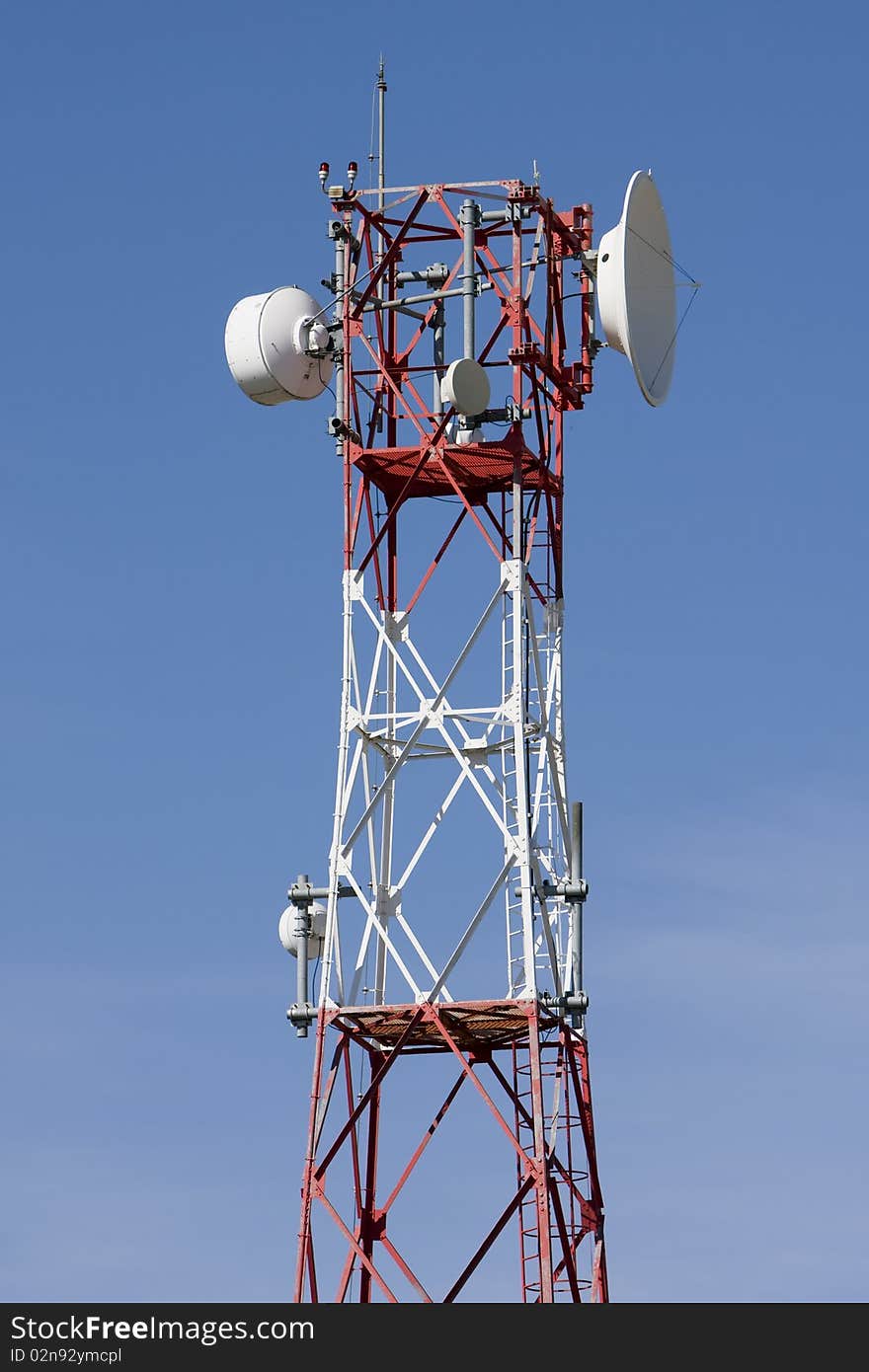 Red and white tower of communications with with a lot of different antennas under clear sky.