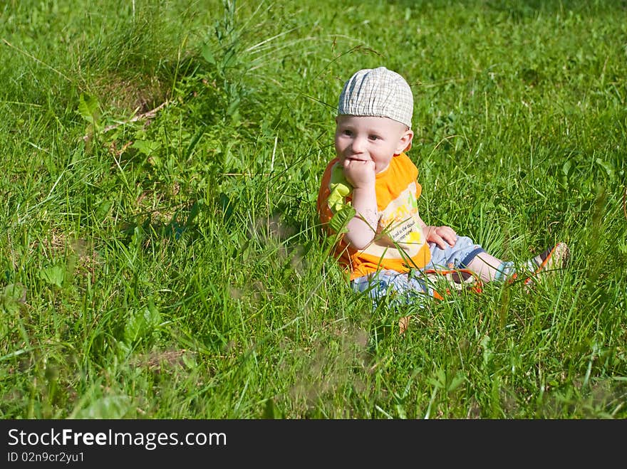 Beautiful little boy looks in green summer meadow