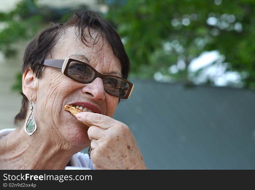 An old lady is using her new teeth to bite something delicious. An old lady is using her new teeth to bite something delicious