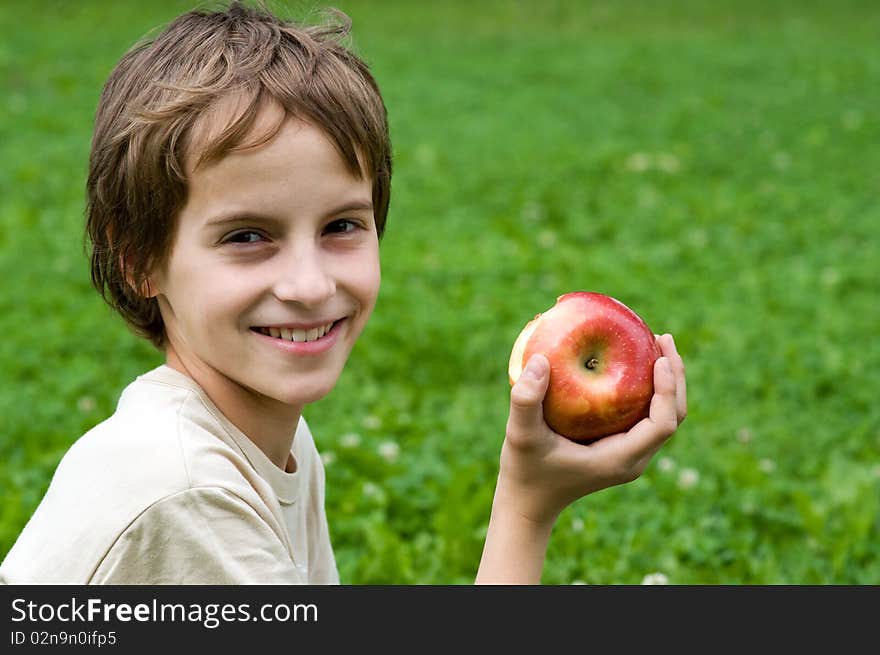 Portrait of a preteen boy with a apple in his hand and green grass in the background. Portrait of a preteen boy with a apple in his hand and green grass in the background