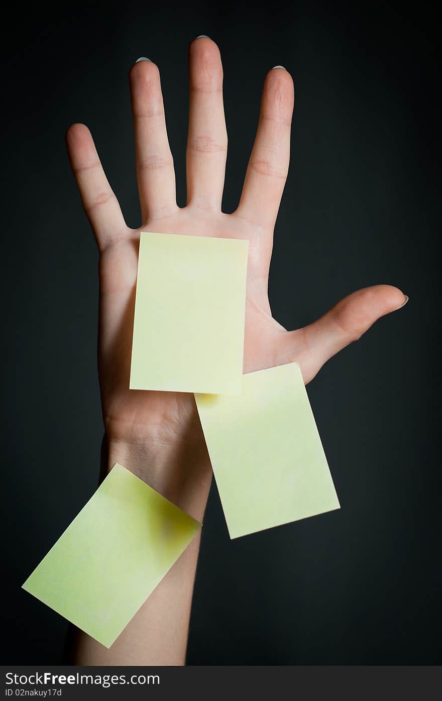 Female hand with three office sticky notes on dark background . All notes are blank and yellow. Female hand with three office sticky notes on dark background . All notes are blank and yellow