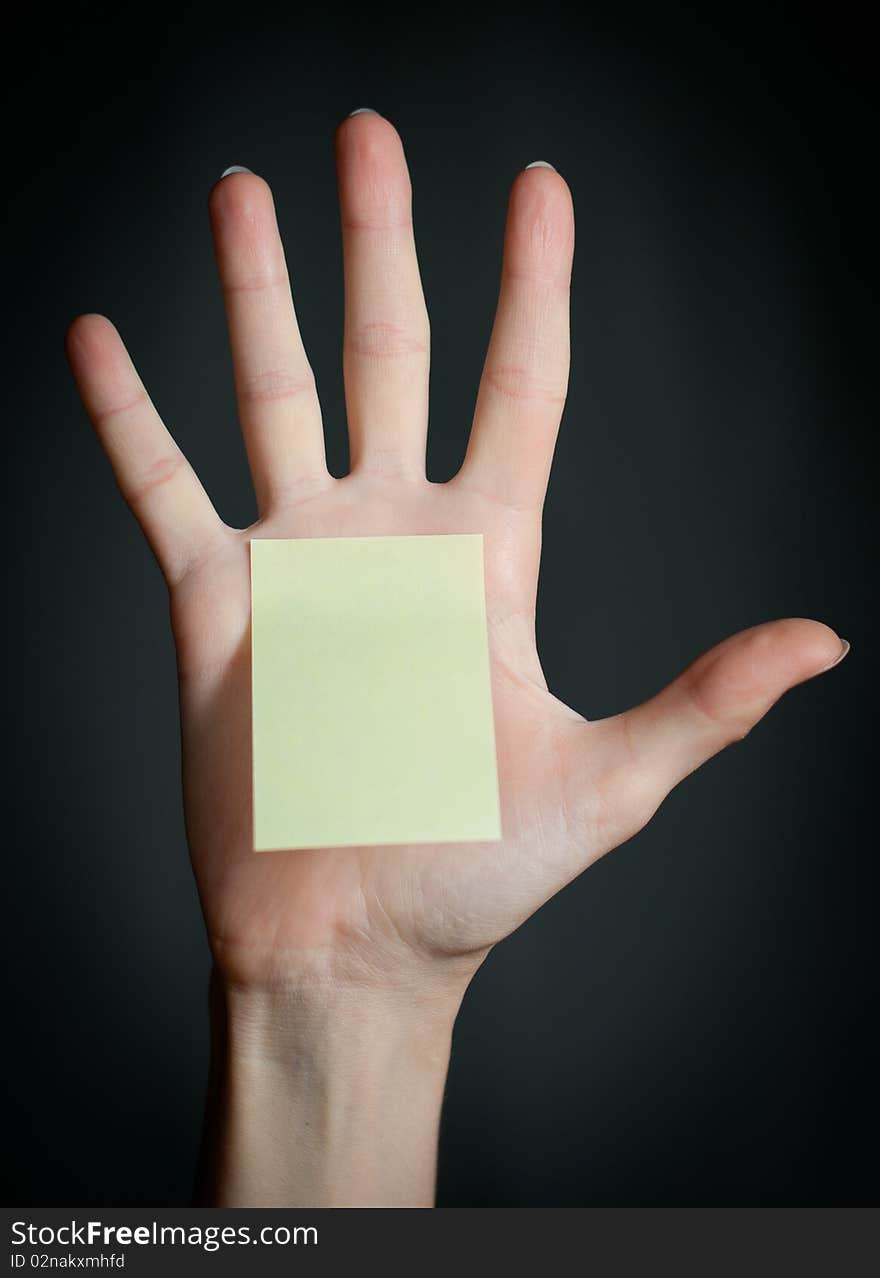 Female hand with sticky office note on dark background . Note is blank and yellow. Female hand with sticky office note on dark background . Note is blank and yellow