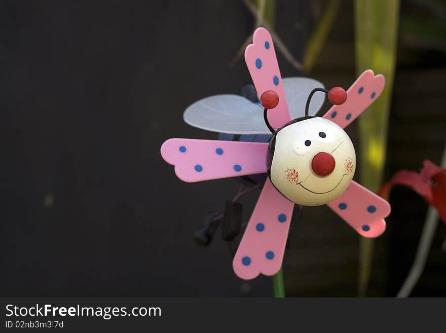 A child's plastic plant pot toy decoration of a stylised bee with pink wings. Set in a garden flower pot. A child's plastic plant pot toy decoration of a stylised bee with pink wings. Set in a garden flower pot.