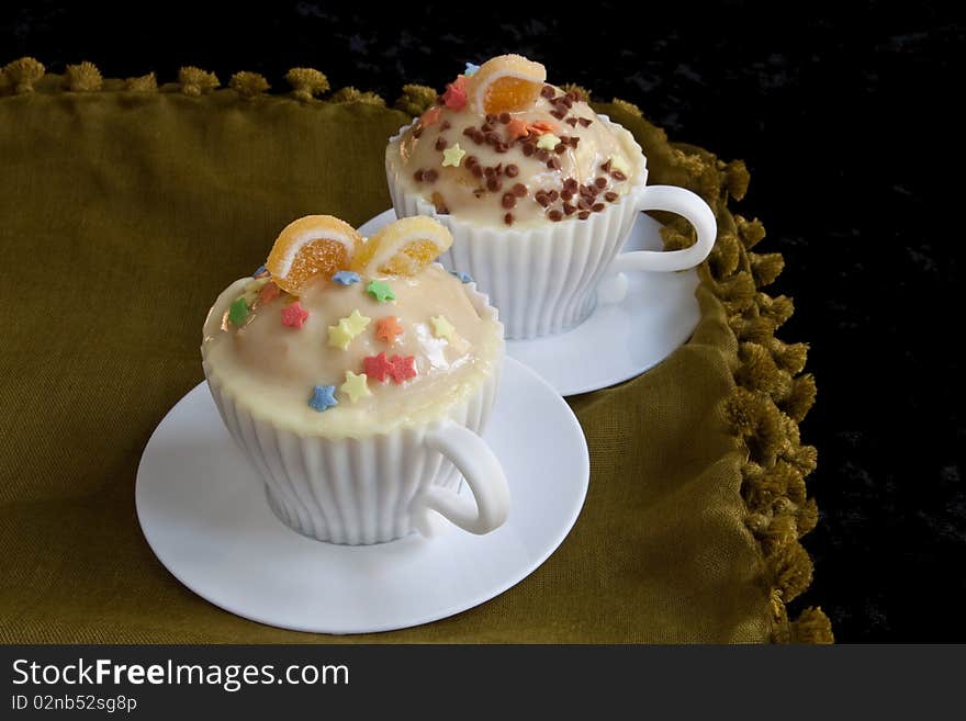 Decorated cupcakes in white teacup molds against a black background. Decorated cupcakes in white teacup molds against a black background