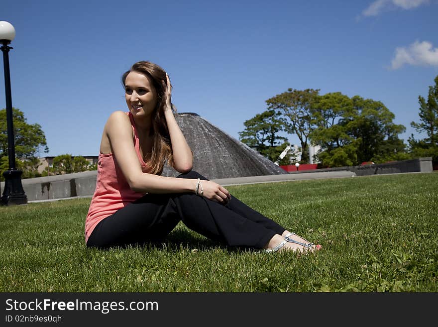 A woman playing with her hair while she is sitting on the grass on a beautiful day in the park. A woman playing with her hair while she is sitting on the grass on a beautiful day in the park.