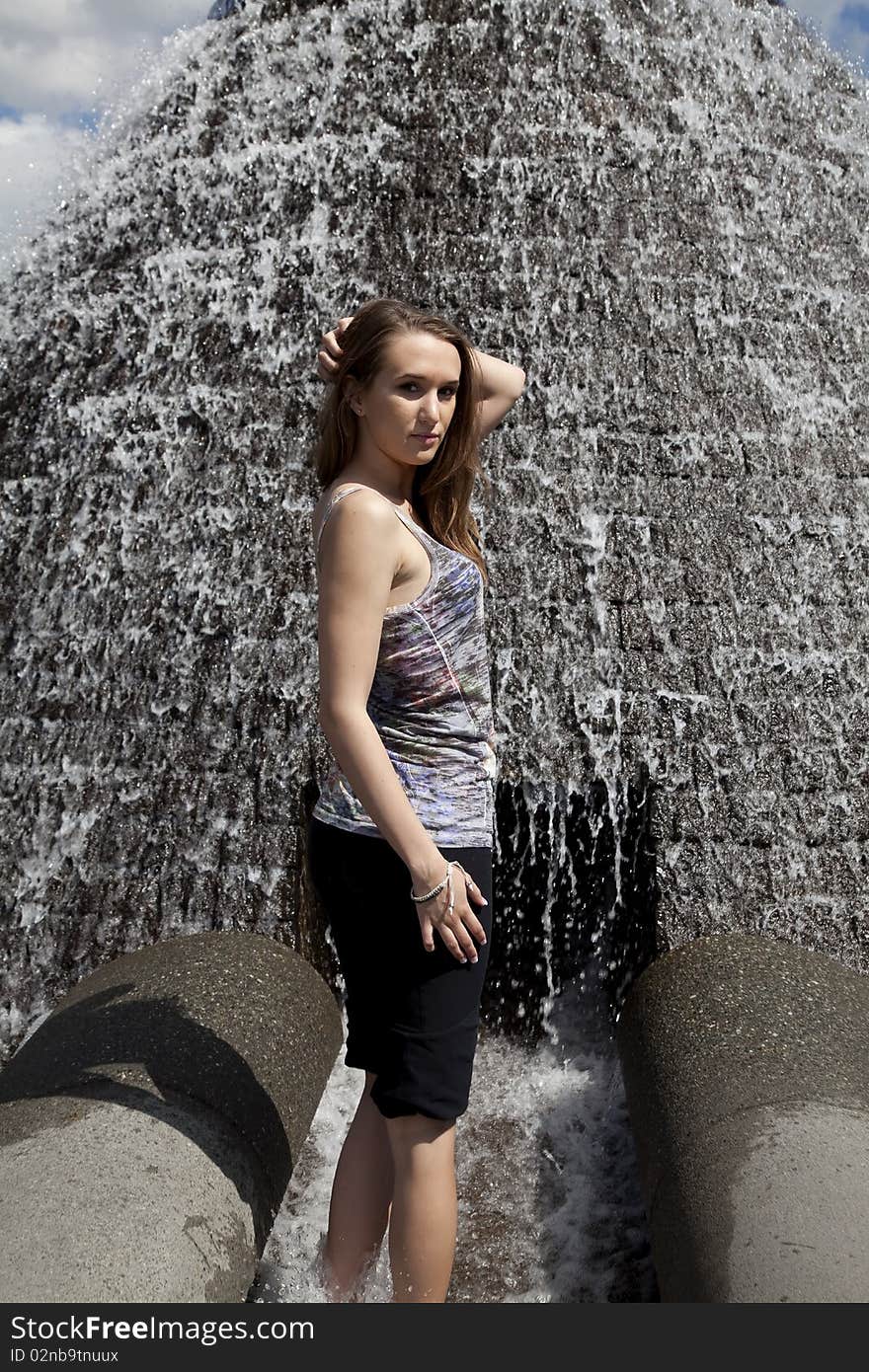 A woman playing in the waterfall in the outdoors while she lifts up her hair to cool off. A woman playing in the waterfall in the outdoors while she lifts up her hair to cool off.