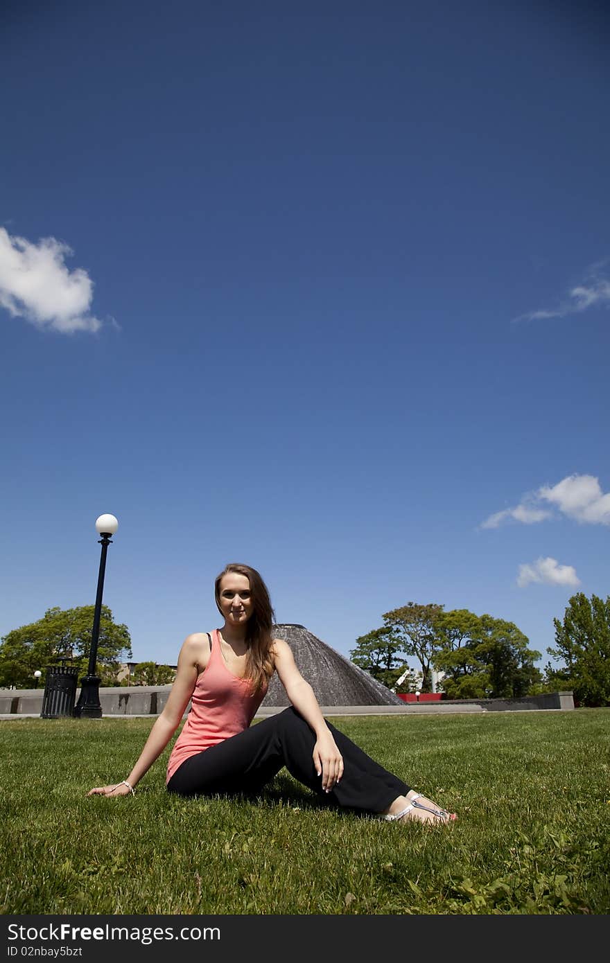 A woman sitting in a park with a beautiful blue sky and nice green grass. A woman sitting in a park with a beautiful blue sky and nice green grass.