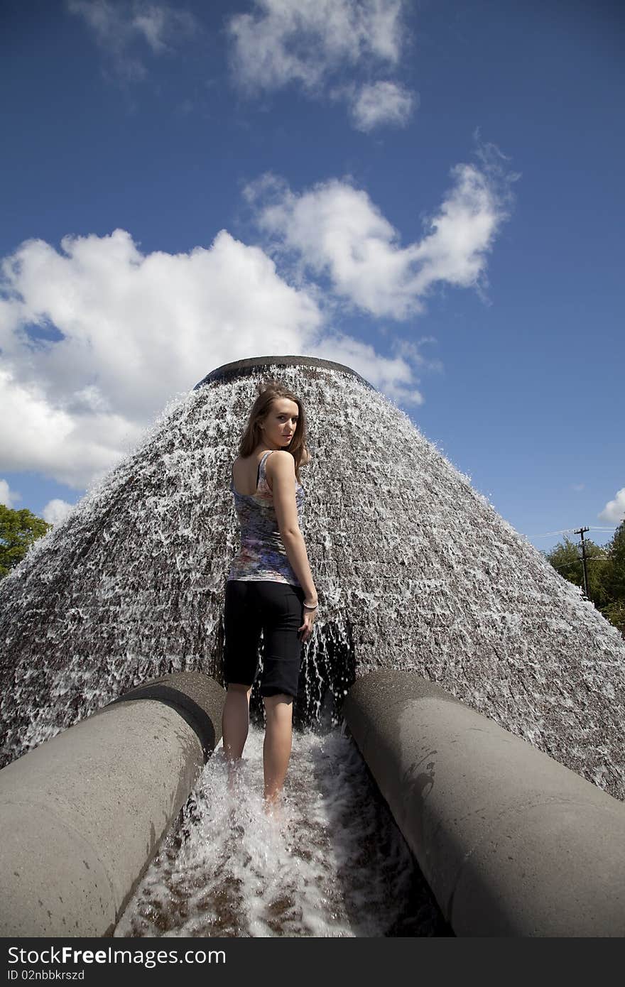 A woman standing in water by a waterfall in the park with a serious expression on her face.