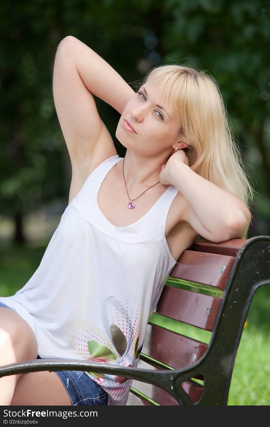 Pretty  blond woman sits with raised arms on park