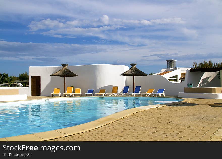 Swimming pool with lounge chairs and thatched umbrellas. Swimming pool with lounge chairs and thatched umbrellas