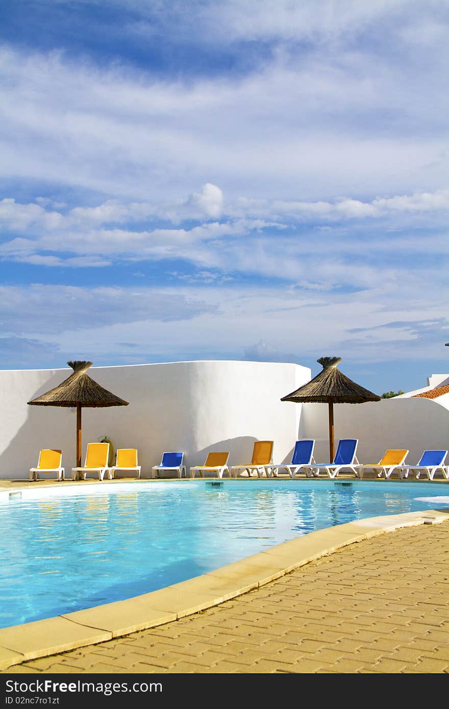 Swimming pool with lounge chairs and thatched umbrellas. Swimming pool with lounge chairs and thatched umbrellas