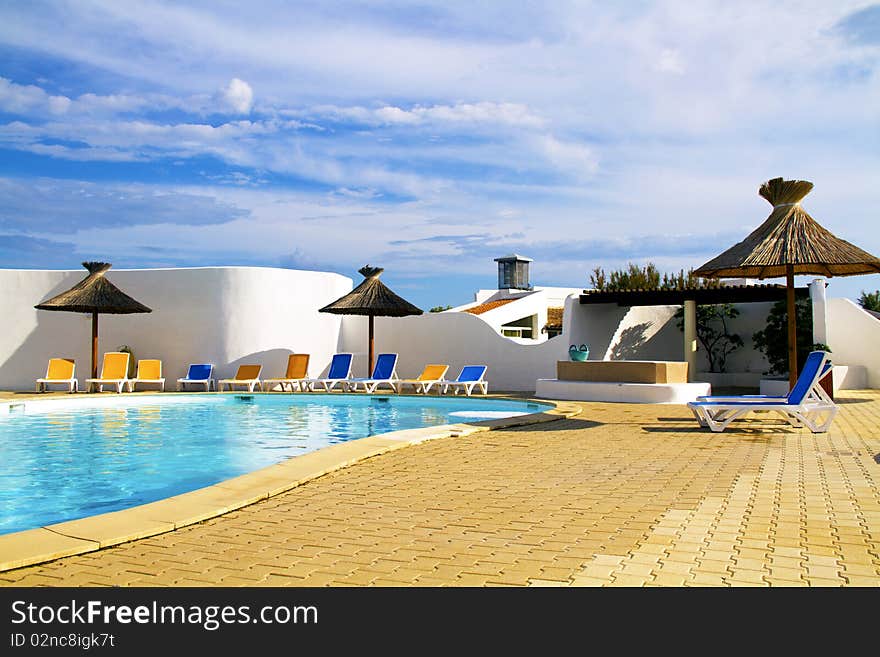 Swimming pool with lounge chairs and thatched umbrellas. Swimming pool with lounge chairs and thatched umbrellas